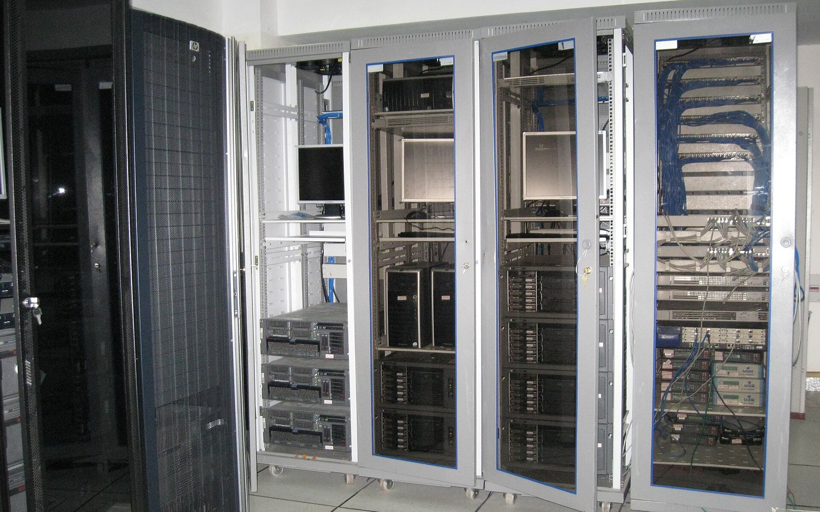 Rows of glass-fronted server cabinets with mounted monitors and cabled network switches in a data center